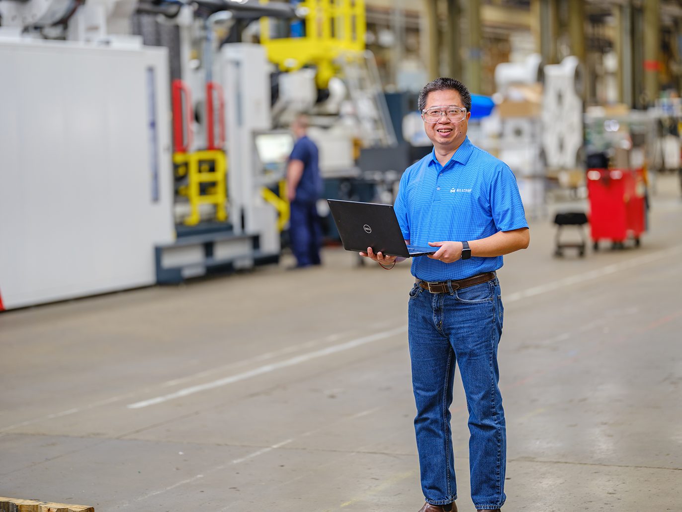 A Milacron process engineer smiling and holding a laptop computer on our production floor.