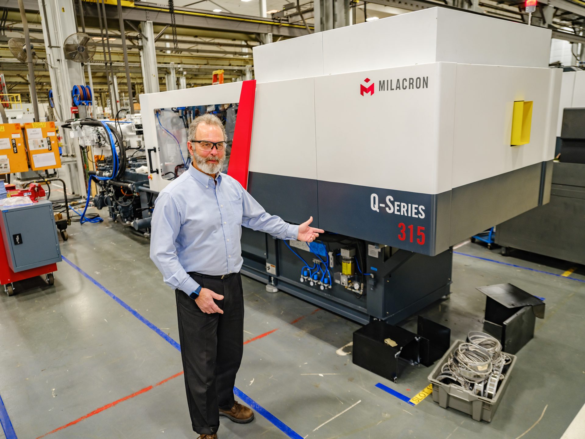 A Milacron product engineer in front of a 315 ton Q-Series injection molding machine demonstrating its high-performance features.