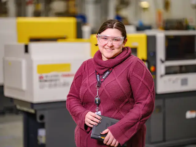 Milacron employee smiling with safety glasses and notebook